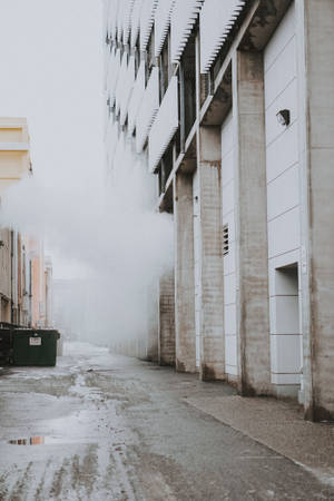 霧氣瀰漫的都市小巷，濕漉漉的路面和現代混凝土建築物。