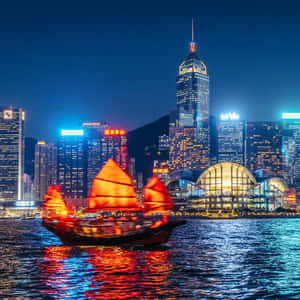 傳統中式帆船在夜間城市燈光下行駛，水面倒映光影。 — 夜景城市 壁紙