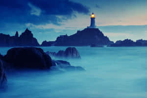 黃昏時岩石島上發光的燈塔與霧氣瀰漫的海浪。