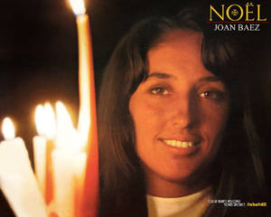 Joan Baez 在黑暗環境中點燃的蠟燭旁微笑。 — 專輯封面 壁紙