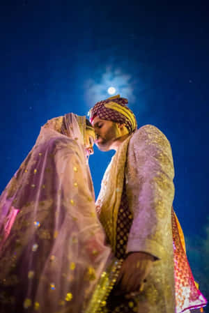 穿著傳統印度婚禮服飾的新娘和新郎在月亮下接吻。