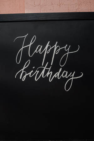 Happy Birthday 以白色草書寫在黑色黑板上。