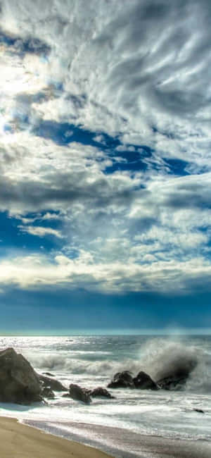 在戲劇性的多雲天空下，海浪拍打著岩石。 — Galaxy A54 壁紙