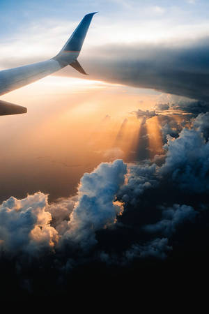 飛機機翼視角，夕陽光芒從上方穿透雲層。