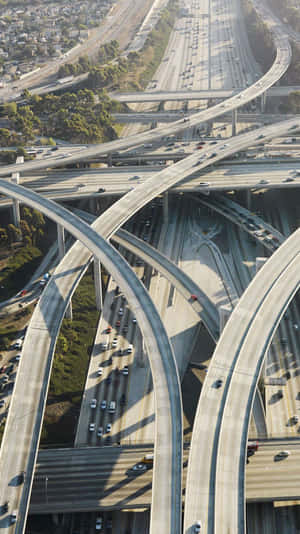 從高空俯瞰一個複雜的高速公路交匯處，擁有彎曲的高架橋和明亮的日光下流暢的交通。