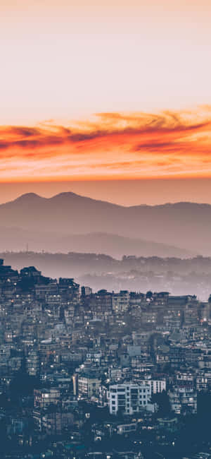 黃昏時分的城市天際線，以橙色雲層和霧氣繚繞的山巒為背景。
