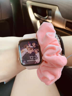 手腕戴粉紅色髮圈和智能手錶，顯示車內K-pop組合照片。