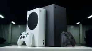 兩部 Xbox 主機連手掣放在白色桌子上，在攝影燈光下。