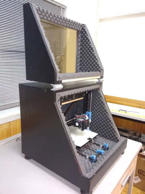 書桌上泡沫內襯外殼內的黑色帶藍色零件的3D打印機。 — 辦公室 壁紙