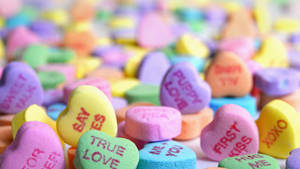 一堆色彩繽紛的心形糖果，上面有甜蜜訊息如 true love 和 puppy love。