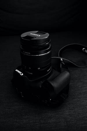 在昏暗燈光下，帶有鏡頭蓋的黑色Canon相機放在有紋理的布料上。