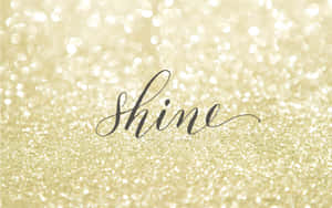 金色閃粉背景上的黑色草書「shine」一詞。