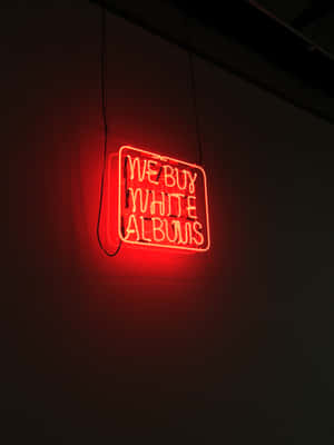 掛在黑暗房間中的紅色霓虹燈牌，上面寫著「We Buy White Albums」。