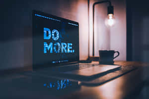 手提電腦屏幕顯示「DO MORE.」，夜晚有溫暖的燈和咖啡杯在附近。