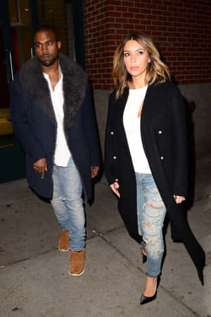 Kanye West 和 Kim Kardashian 晚上在城市行人道上穿著冬季外套和牛仔褲行走。