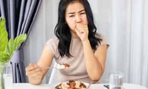 女士在餐桌前拿著一匙食物並捂住嘴巴。