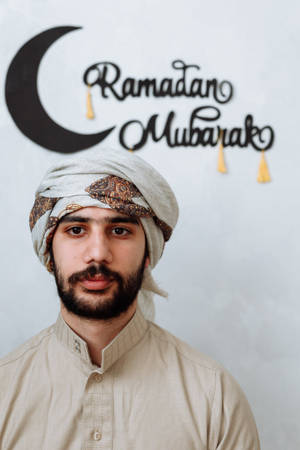 男子戴著傳統頭巾，身穿米色襯衫，身後有Ramadan Mubarak新月裝飾。 — 齋戒月 壁紙