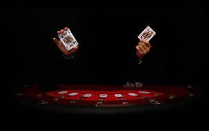 兩隻手在帶有籌碼的紅色遊戲桌上高舉撲克牌。