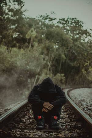 一個穿著黑色連帽衫的人獨自坐在霧氣森林中的火車軌道上。
