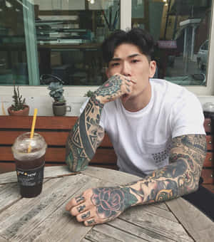 有紋身的男人坐在戶外咖啡桌旁喝飲料。 — 紋身 壁紙