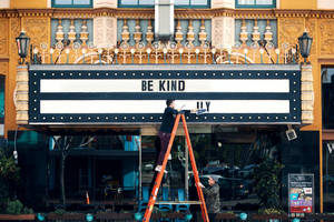 工人在華麗金色外牆的劇院招牌上安裝「BE KIND」。 — 復古gif 壁紙
