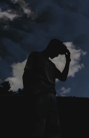 一個人的剪影，在黑暗的多雲天空下抱著頭。