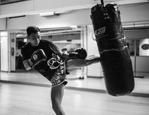 男子在健身房用重型沙袋練習踢拳。