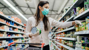 戴著口罩和手套的女性在超市通道中選購罐頭食品。