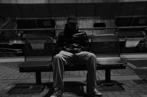 一個穿著羽絨外套的男人獨自坐在火車站的長椅上。 — 黑白 壁紙