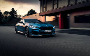 藍色BMW M8 Coupe在黃昏時高速駛過現代建築。