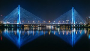 一座藍色燈光的現代橋樑在夜晚平靜的水面上完美倒映。 — 建築 壁紙