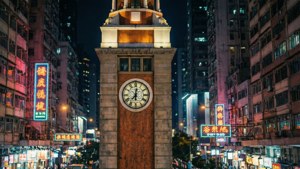 一座歷史悠久的鐘樓在密集的城市夜景中閃耀，伴隨著霓虹燈招牌和高樓大廈。 — 香港 壁紙