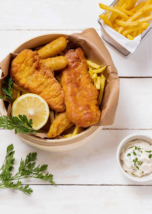 酥脆炸魚薯條配檸檬、歐芹和塔塔醬，置於白色木上。