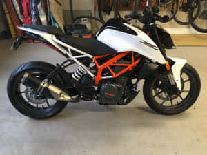 白色和橙色的KTM 390電單車停放在車庫中，牆上掛著單車。