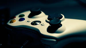 白色 Xbox 360 控制器，帶有彩色按鈕和黑色搖桿，在昏暗的藍光中。
