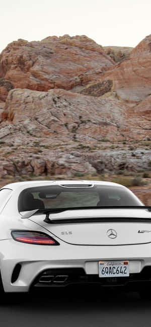 白色 Mercedes SLS AMG 在日落時分疾馳穿過紅色岩石沙漠峽谷。 — Galaxy M56 壁紙