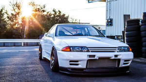 白色日產Skyline GT-R在日落時停泊在堆疊輪胎附近。