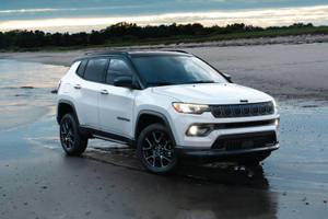 白色Jeep Compass SUV在日落時停泊在濕沙灘上