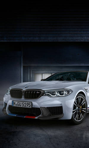 銀色BMW M5跑車停放在光線昏暗的車庫中，帶有工業捲簾門。