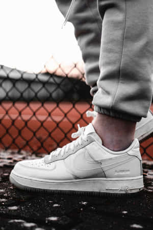 白色Nike Air Force 1運動鞋在濕漉漉的人行道上靠近鐵絲網圍欄。