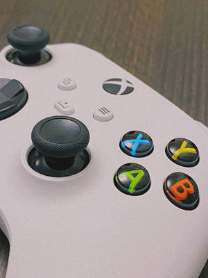 白色Xbox手掣，帶有彩色按鈕，放置在木質表面上。 — Xbox GIF 壁紙