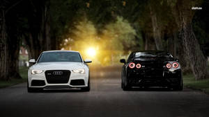 日落時分，兩輛豪華跑車在一條林蔭大道上相對而行。 — Audi R8 GIF 壁紙