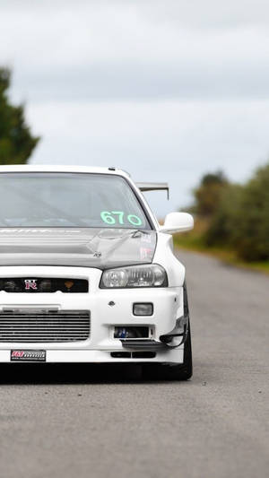白色日產Skyline R34賽車，號碼670，停泊在鄉村道路上。 — 天際線 壁紙