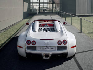 白色Bugatti Veyron Grand Sport開篷車停泊在現代玻璃建築附近。