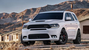 白色Dodge Durango SRT SUV停泊在沙漠建築附近的碎石路上，背景有山脈。 — 汽車 壁紙