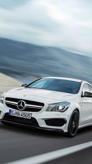 白色Mercedes跑車在日落時分於海岸公路上飛馳。