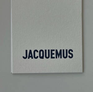 灰色紋理筆記本，帶有海軍藍色 JACQUEMUS 文字。