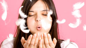 女性在粉紅色背景前吹白色羽毛