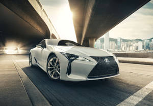 白色Lexus跑車在日落時分於城市高架橋下行駛。