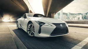 白色Lexus跑車在日落時分行駛於城市高架橋下。